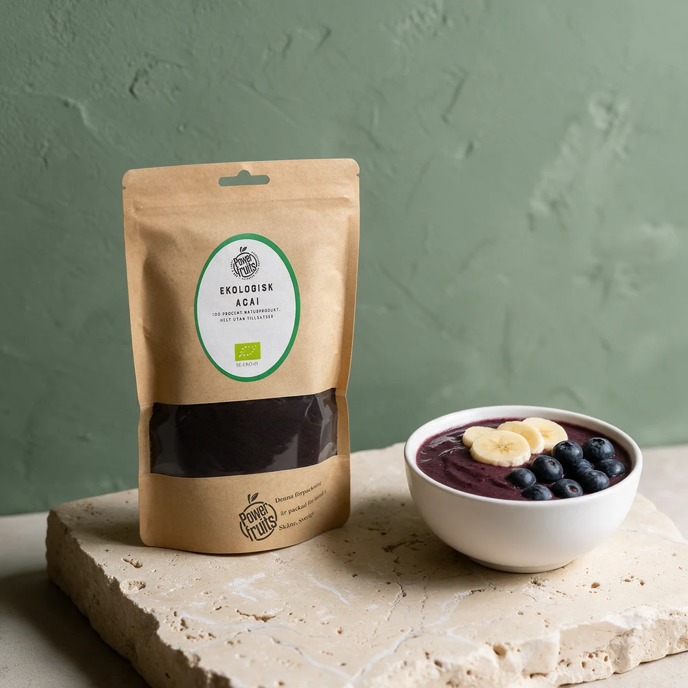Powerfruits Økologisk Acai, posen på 200 gram med vindu mot det mørke pulveret, og en acai bowl med banan og blåbær