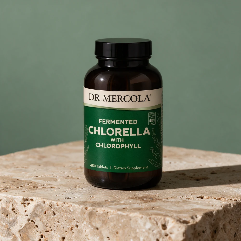 Dr. Mercola Fermented Chlorella i en mørkebrun flaske med svart lokk og grønn etikett på en travertinblokk
