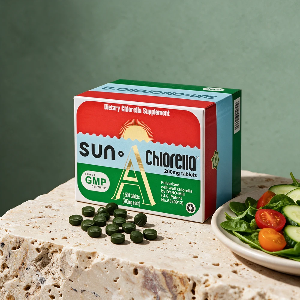 Sun Chlorella-esken i rødt, blått og grønt med en stigende sol og noen mørkegrønne tabletter foran, ved en tallerken med salat på en travertinblokk