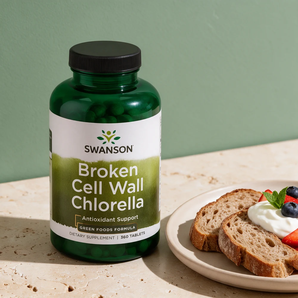 Swanson Broken Cell Wall Chlorella i en grønn gjennomsiktig flaske med svart lokk ved en tallerken med brød, yoghurt og bær på en travertinblokk