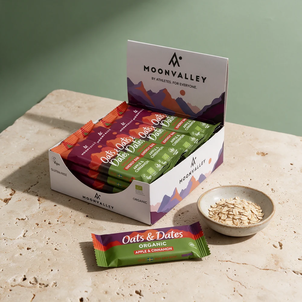 Moonvalley Oats & Dates Apple & Cinnamon, åpen eske og én bar, ved havregryn