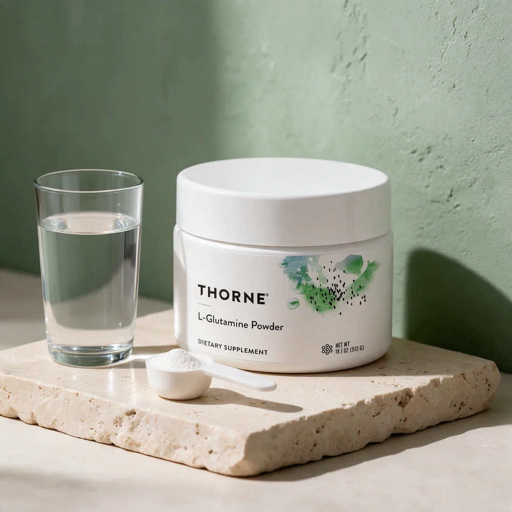 Thorne L-Glutamine Powder, lav hvit boks på 513 g, med en hvit scoop pulver og et høyt vannglass