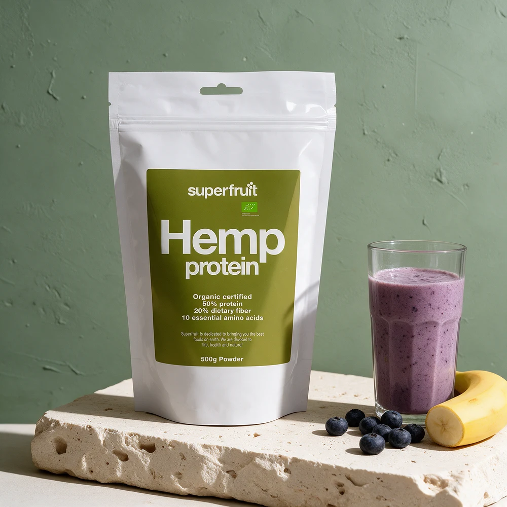 Superfruit Hemp protein, hvit pose med grønn etikett «50% protein», og et glass blåbærsmoothie med banan
