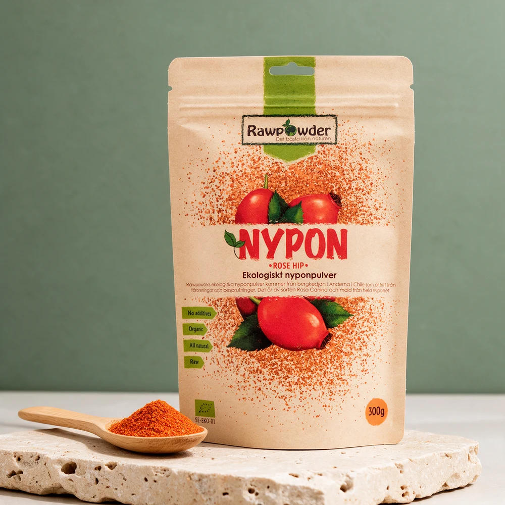 Rawpowder Nypepulver, kraftpapirpose på 300 g med tegnede nyper og teksten «NYPON», ved en full spiseskje med oransjerødt pulver