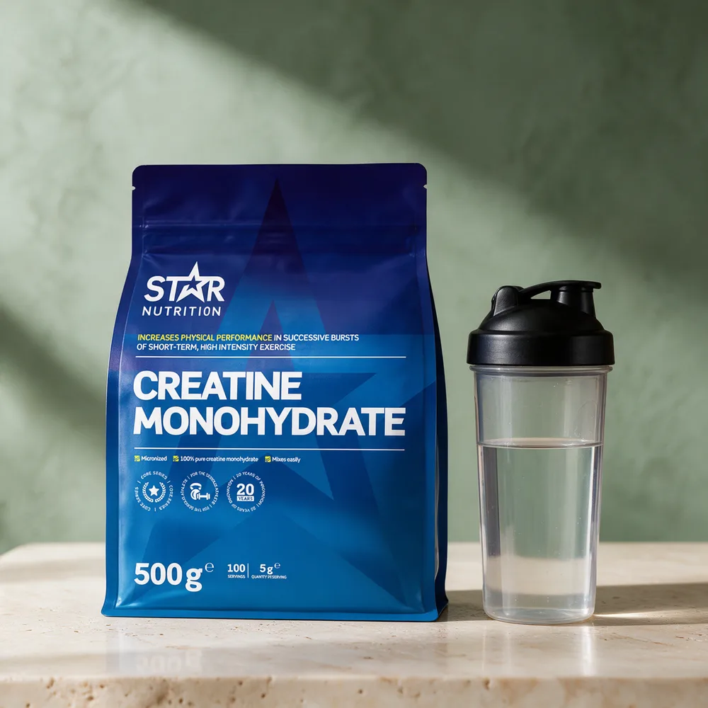 Star Nutrition Creatine Monohydrate i blå, stående pose på 500 gram ved siden av en shakerflaske med vann