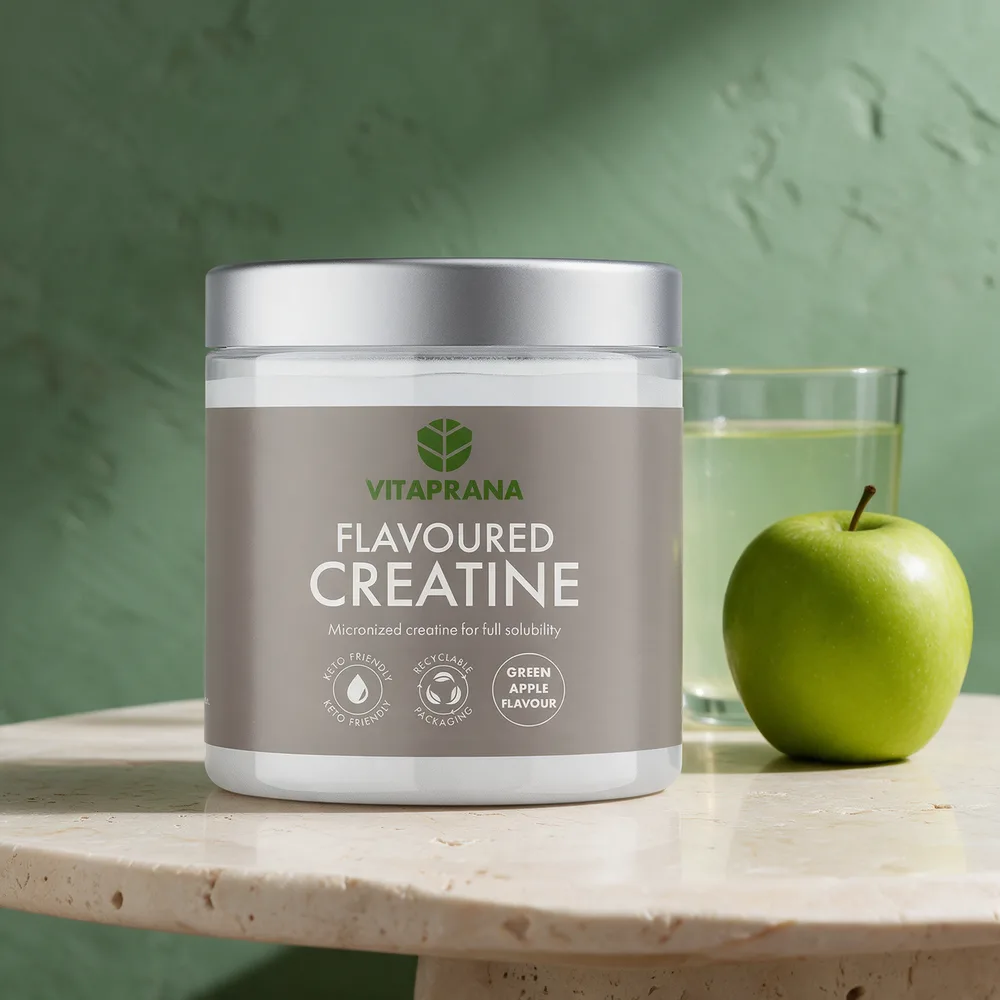 Vitaprana Flavoured Creatine med eplesmak, boks med grå etikett og sølvfarget lokk, ved siden av et grønt eple og et drikkeglass med lysegrønn drikk