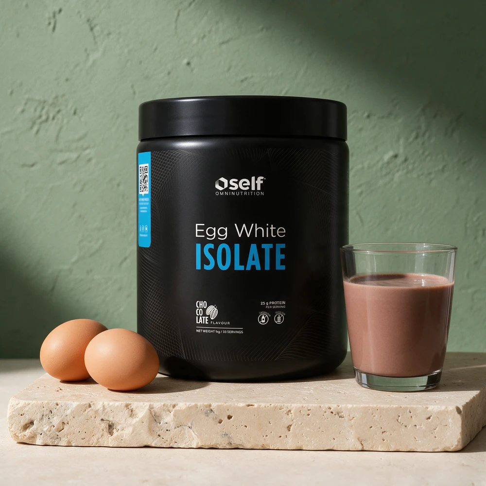 Self Omninutrition Egg White Isolate med sjokoladesmak i svart boks ved to egg og et glass sjokoladedrikk