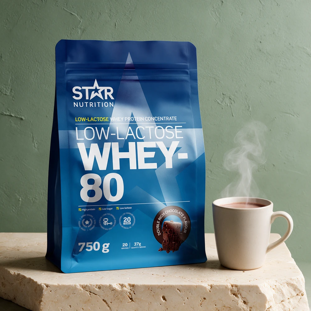 Star Nutrition Low-Lactose Whey-80 Double Rich Chocolate i blå pose ved en kopp varm drikk