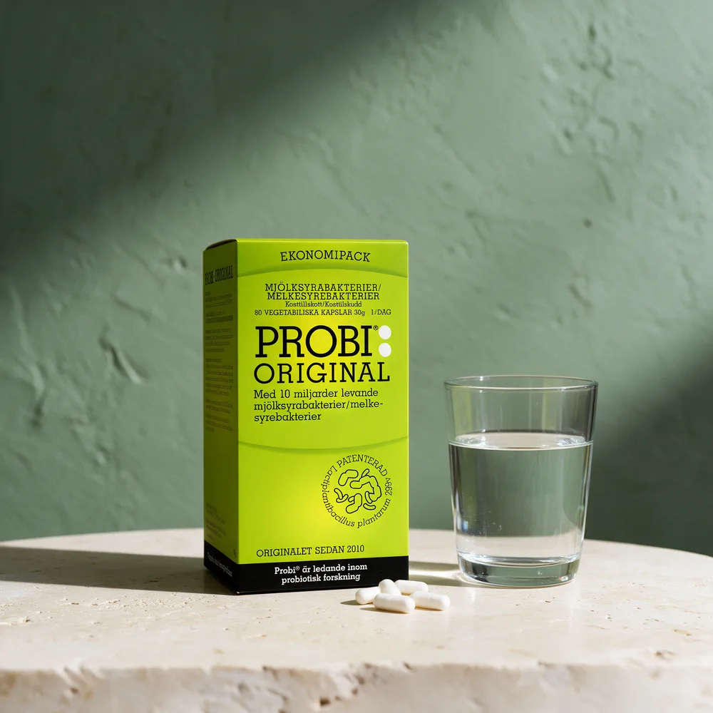 Probi Original, eske med 80 vegetabilske kapsler, med noen kapsler og et glass vann ved siden av
