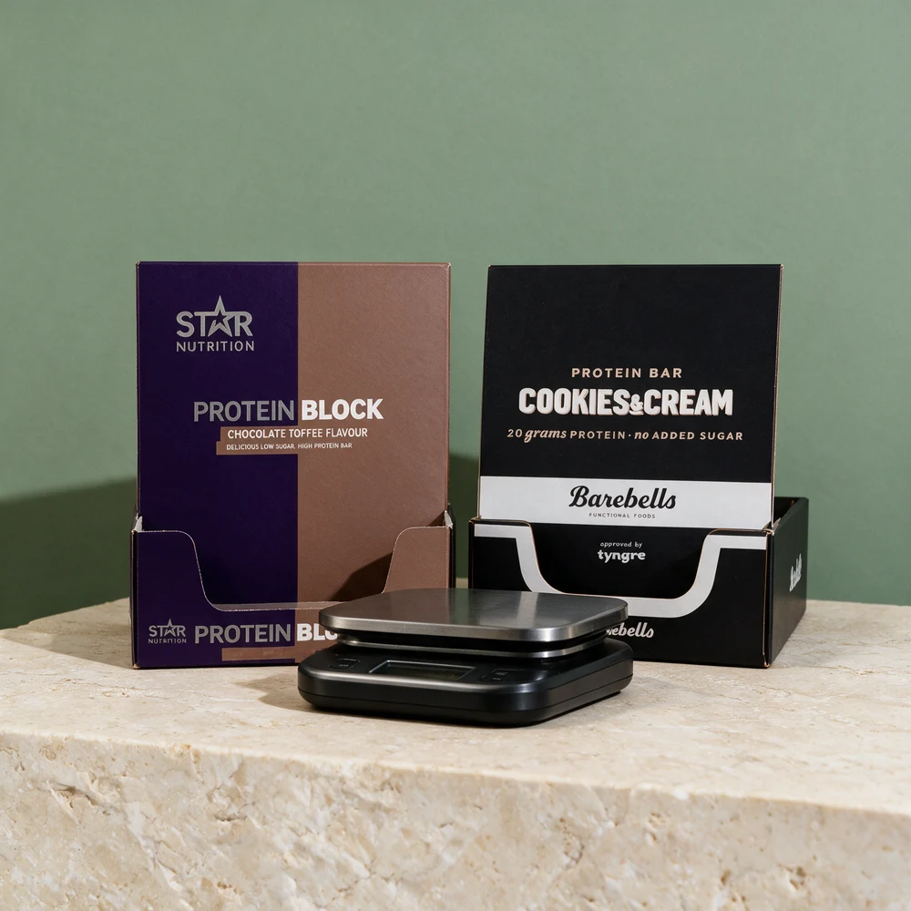 Eskene til Star Nutrition Protein Block og Barebells Protein Bar Cookies & Cream med en kjøkkenvekt foran