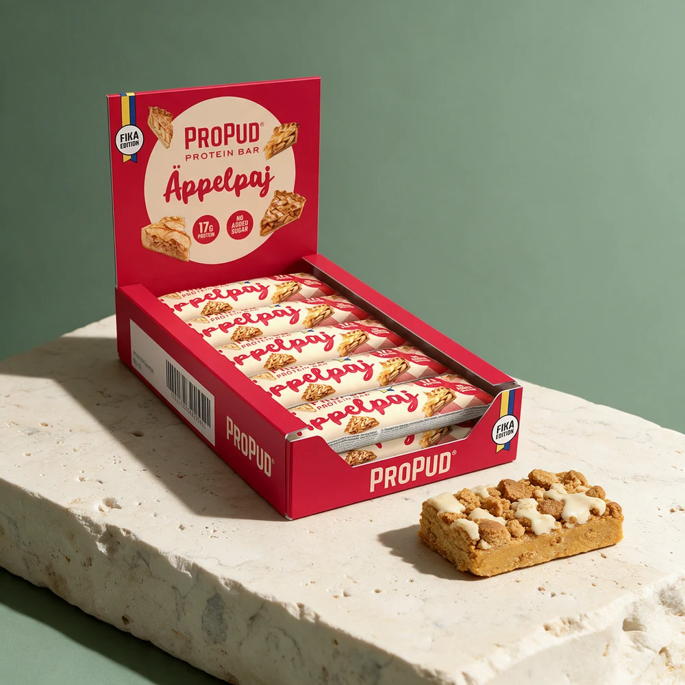 ProPud Protein Bar Äppelpaj i eske og en tykk bar med kakesmuler og hvit glasur på toppen