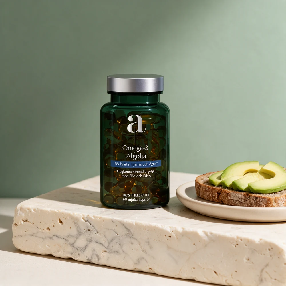 A+ Omega-3 algeolje i mørkegrønn boks med sølvlokk ved en tallerken med brødskive og avokado på et travertinbord