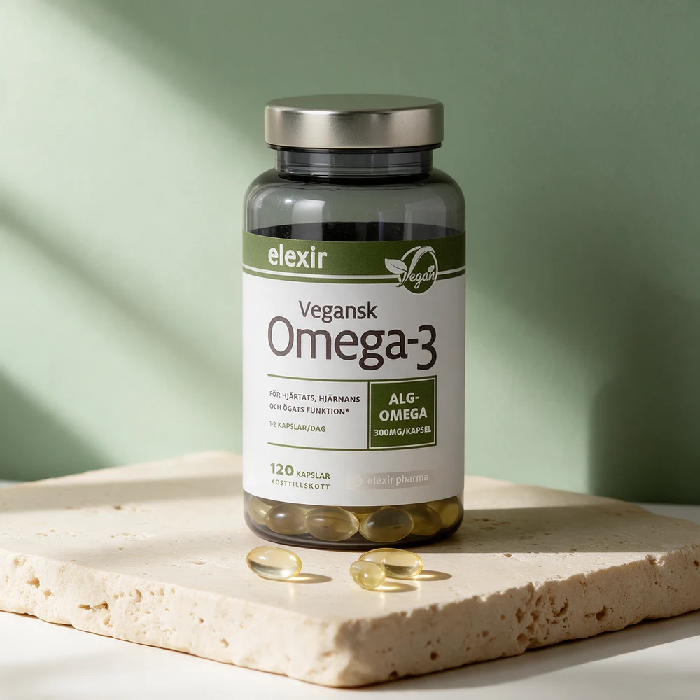 Elexir Pharma Vegansk Omega-3 i røykfarget boks med sølvlokk og olivengrønn etikett, med tre bleke kapsler foran på et travertinbord