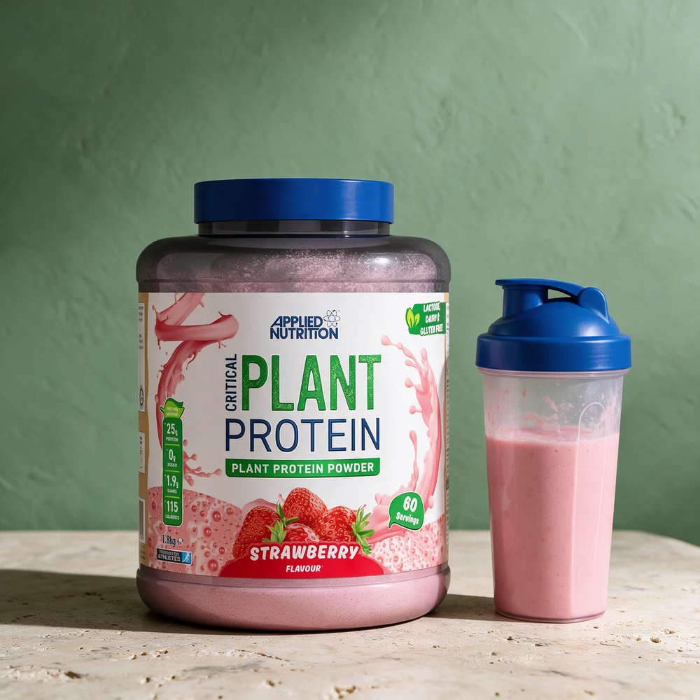 Applied Nutrition Critical Plant Protein med jordbær i stor boks ved en shaker med rosa shake på et travertinbord
