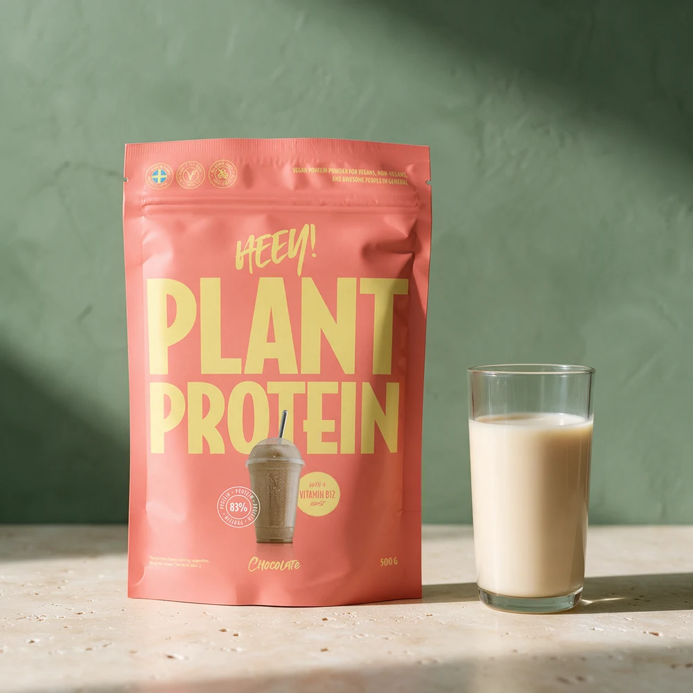 Heey! Vegansk Protein i pose ved et glass havredrikk på et travertinbord