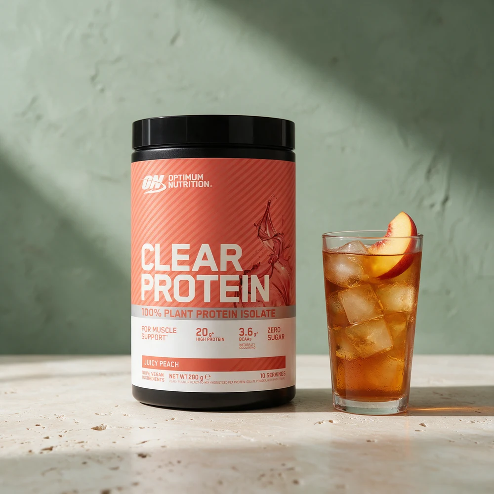 Optimum Nutrition Clear Vegan Protein i boks ved et høyt glass fersken-iste på et travertinbord