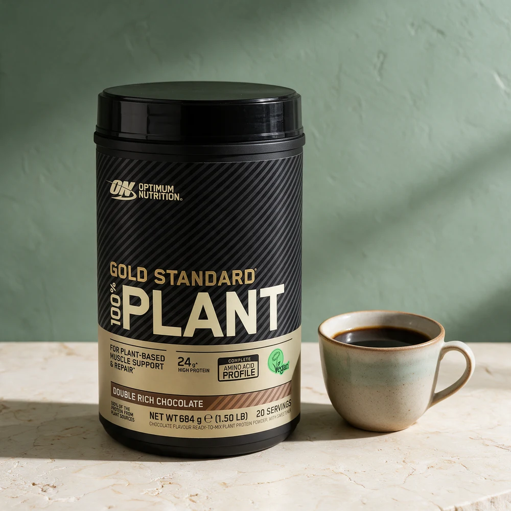 Optimum Nutrition Gold Standard 100% Plant i boks ved en kopp kaffe på et travertinbord