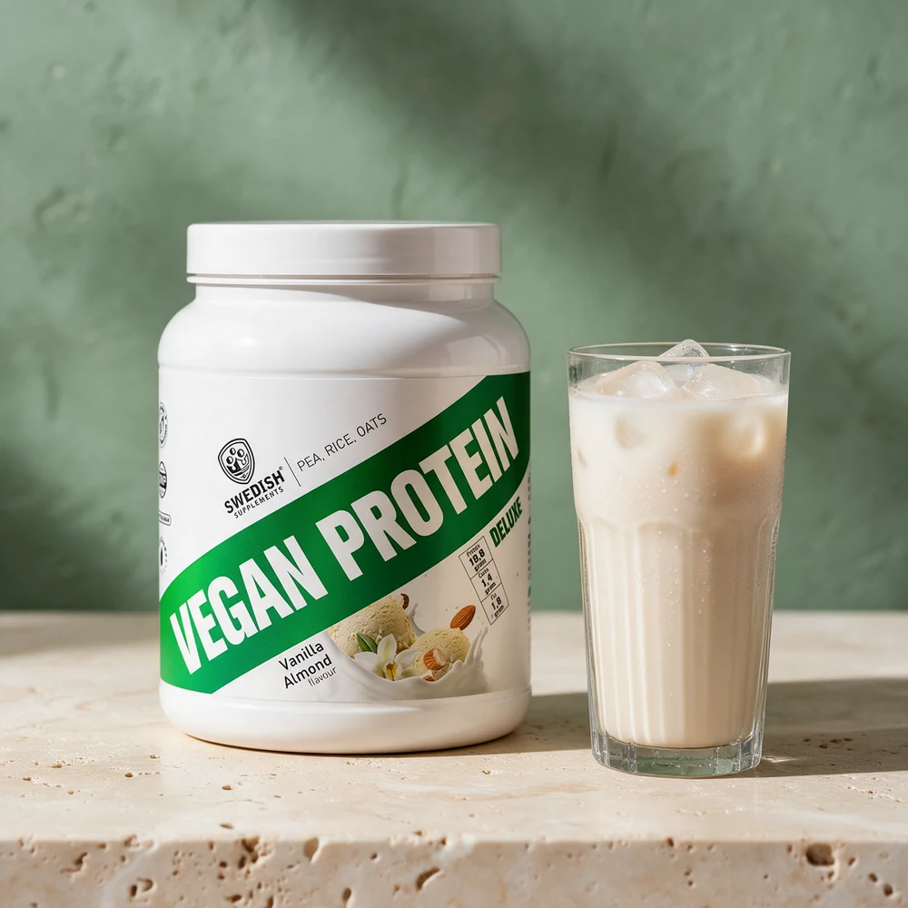 Swedish Supplements Vegan Protein Deluxe i boks ved et glass havredrikk med isbiter på et travertinbord