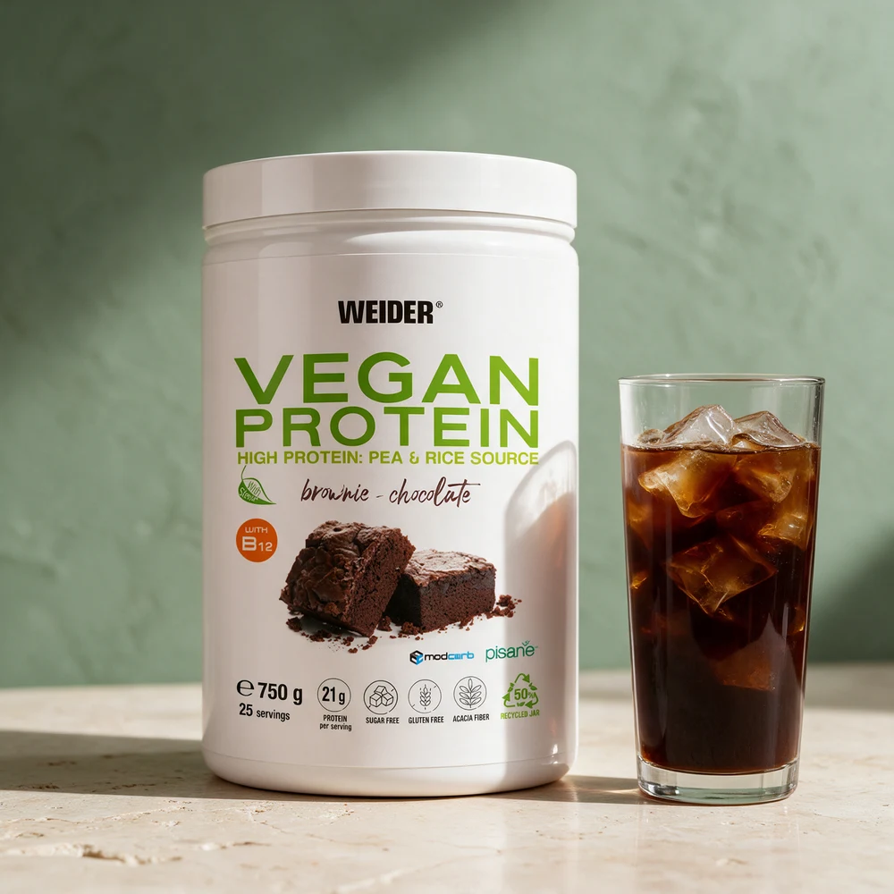Weider Vegan Protein i boks ved et glass iskaffe med kaffeterninger på et travertinbord